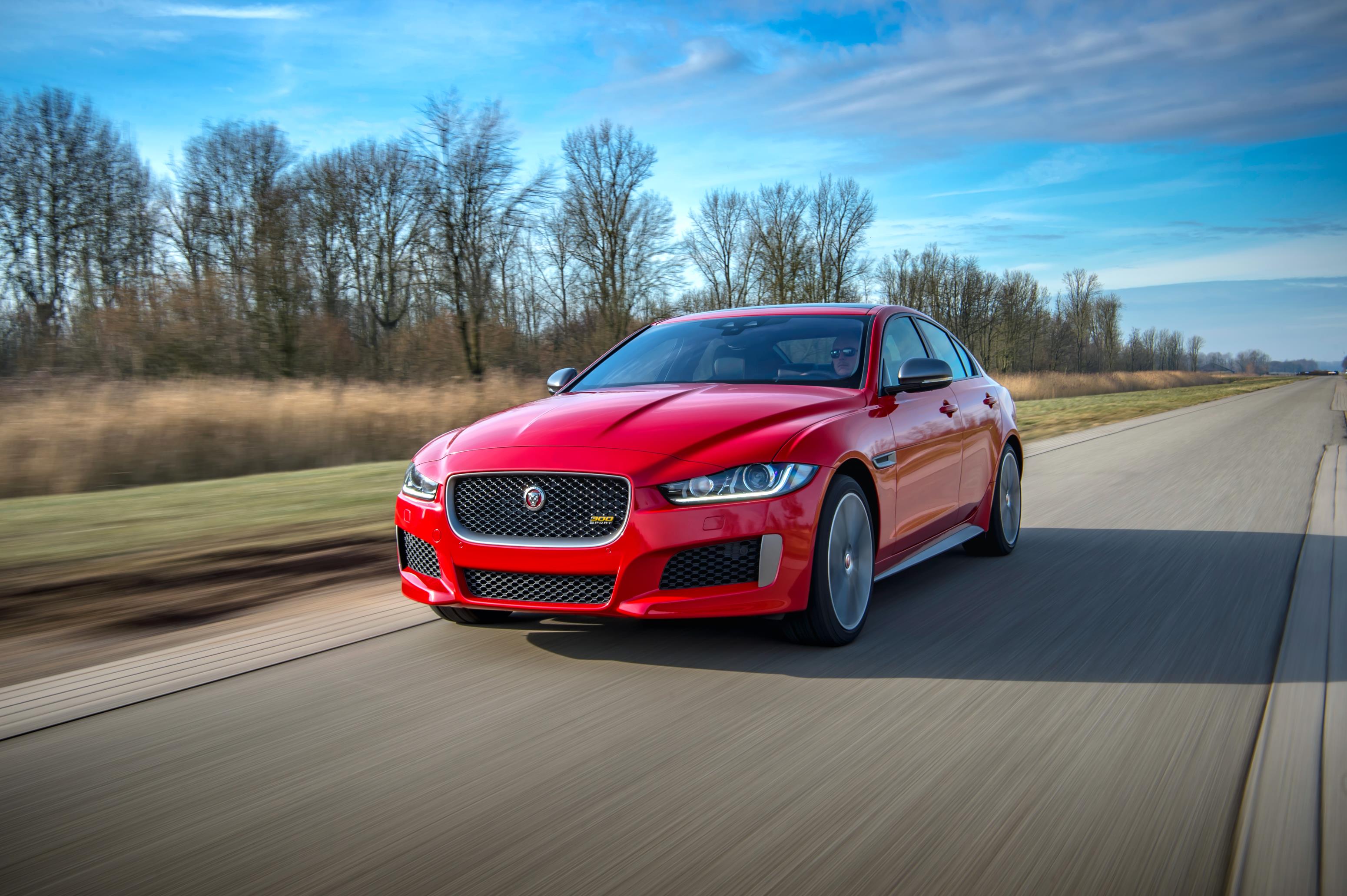 Red Jaguar XE driving towards you with a very blue sky